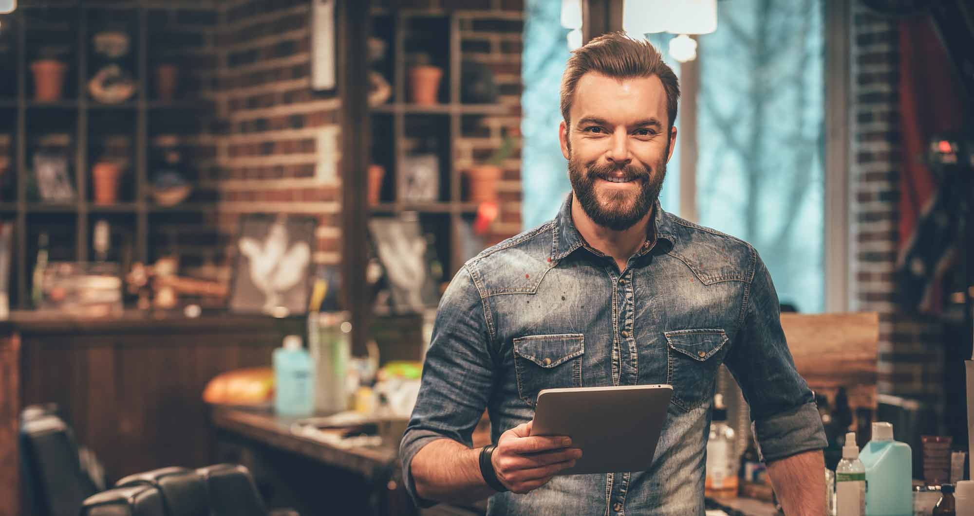 A barber holding a tablet standing in the barbershop
